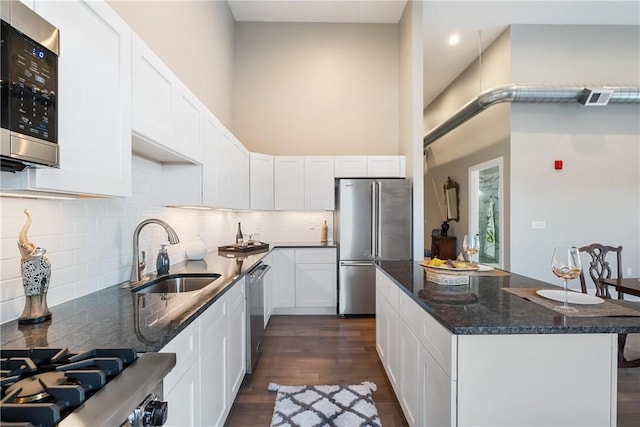 kitchen with a towering ceiling, appliances with stainless steel finishes, sink, and white cabinets