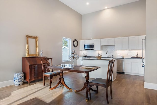 dining room with sink, a towering ceiling, and light wood-type flooring