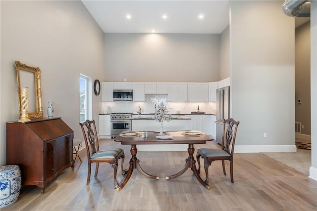 dining area with a towering ceiling and light hardwood / wood-style flooring