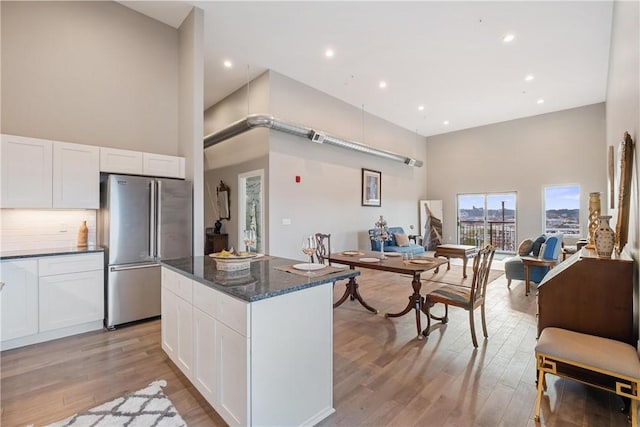 kitchen with stainless steel refrigerator, white cabinetry, dark stone countertops, a high ceiling, and light hardwood / wood-style flooring