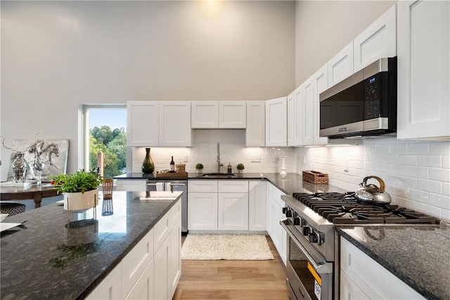 kitchen featuring stainless steel appliances, white cabinetry, sink, and dark stone counters