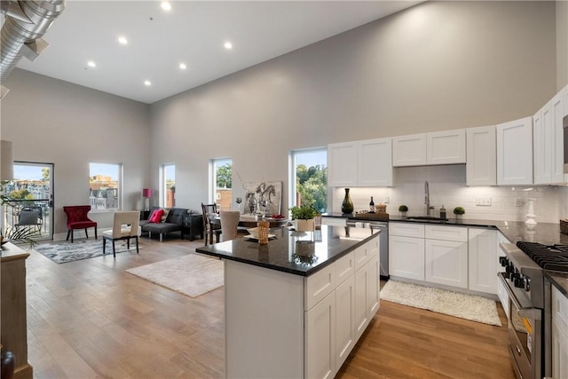 kitchen featuring sink, white cabinets, a high ceiling, stainless steel appliances, and light wood-type flooring