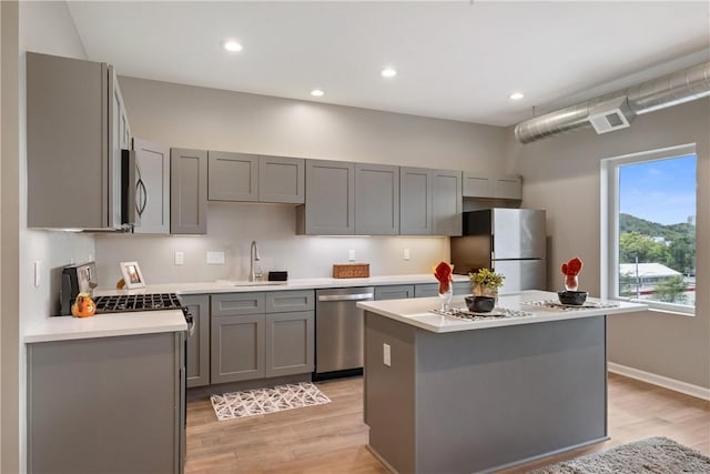 kitchen with appliances with stainless steel finishes, a center island, sink, and gray cabinetry