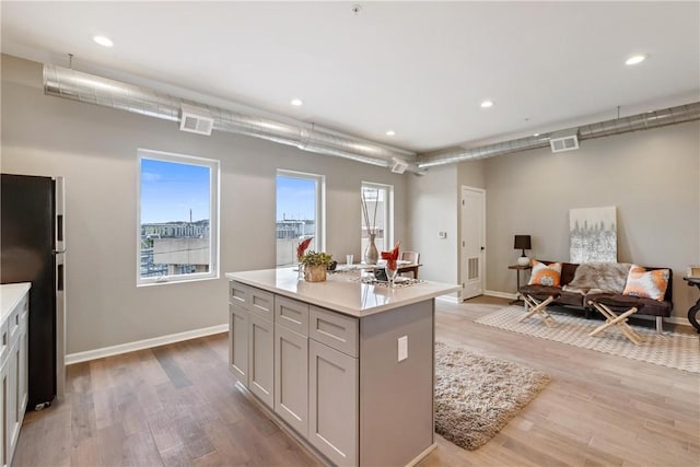 kitchen with stainless steel fridge, gray cabinets, light hardwood / wood-style floors, and a kitchen island