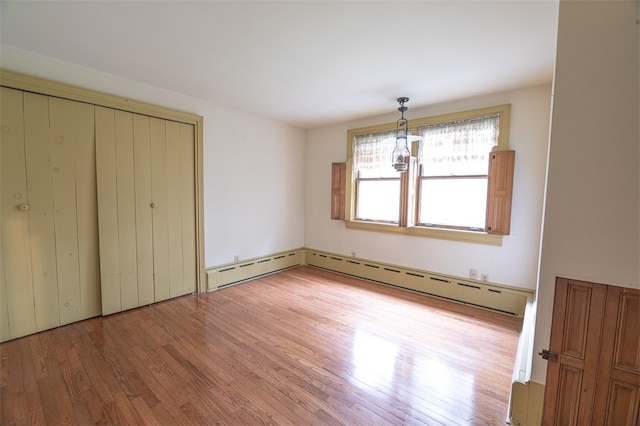 unfurnished bedroom with an inviting chandelier, a closet, a baseboard radiator, and hardwood / wood-style flooring