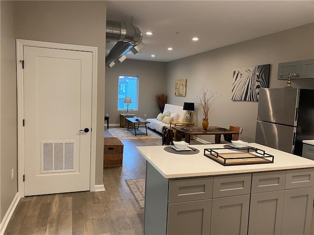 kitchen with gray cabinetry, stainless steel refrigerator, a center island, and dark wood-type flooring