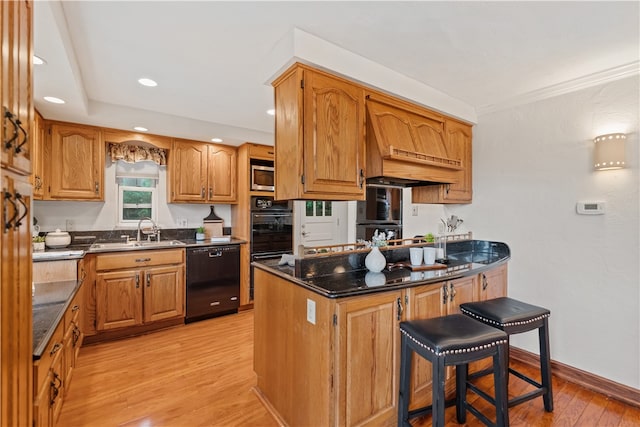 kitchen featuring sink, a kitchen bar, custom exhaust hood, light hardwood / wood-style flooring, and black appliances