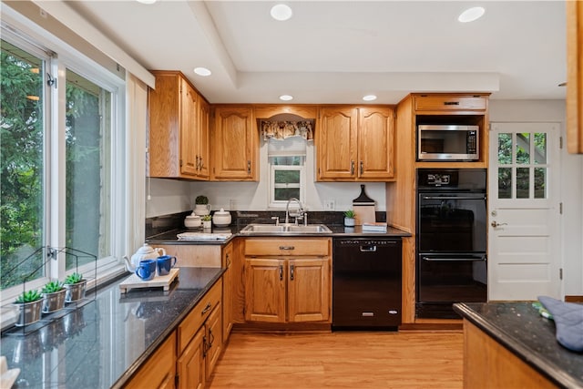 kitchen with dark stone counters, black appliances, light hardwood / wood-style floors, and sink