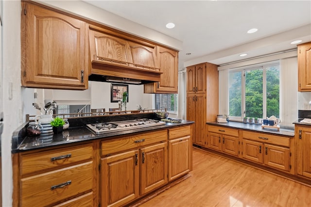 kitchen featuring dark stone countertops, custom exhaust hood, light hardwood / wood-style flooring, and white gas stovetop