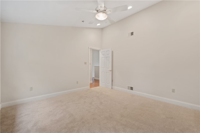 spare room with a towering ceiling, ceiling fan, and light colored carpet