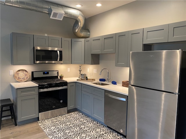 kitchen featuring stainless steel appliances, sink, light wood-type flooring, and gray cabinets