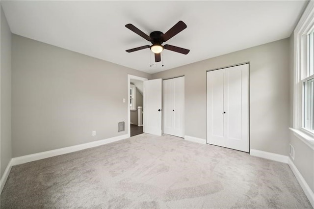 unfurnished bedroom with two closets, ceiling fan, and carpet floors