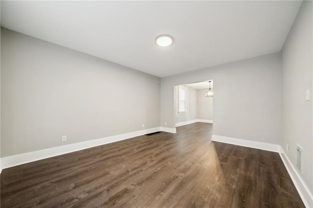 spare room with an inviting chandelier and dark hardwood / wood-style floors