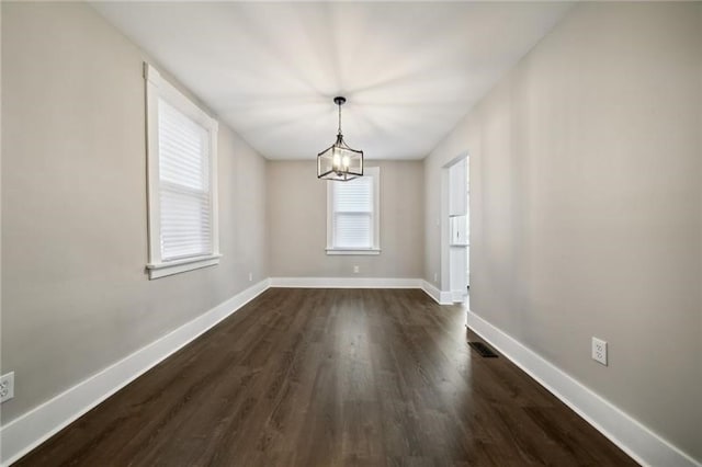 empty room featuring an inviting chandelier and dark hardwood / wood-style flooring