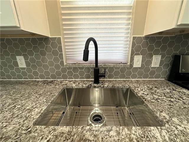 details featuring decorative backsplash, white cabinetry, light stone countertops, and sink