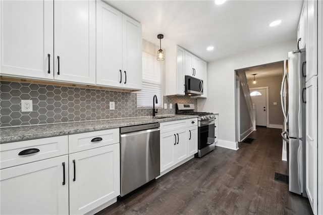 kitchen with appliances with stainless steel finishes, white cabinetry, dark wood-type flooring, decorative light fixtures, and sink