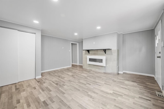 unfurnished living room with wooden walls, a fireplace, and light wood-type flooring