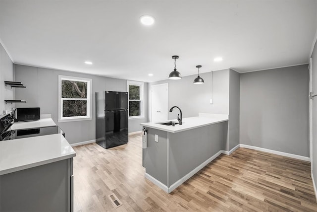 kitchen featuring kitchen peninsula, black appliances, light hardwood / wood-style flooring, decorative light fixtures, and sink