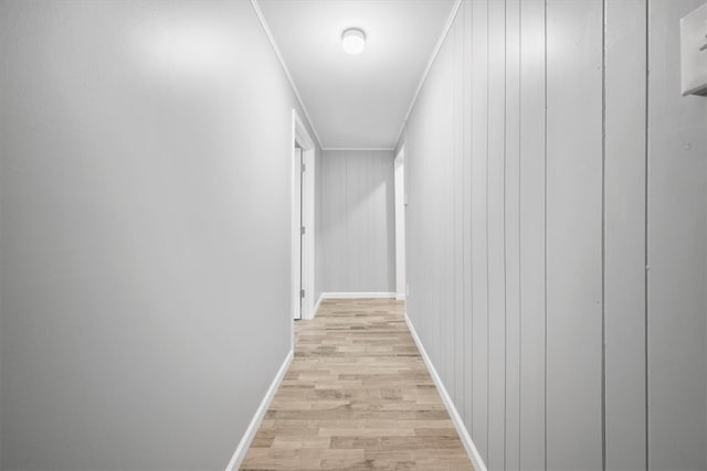 hallway featuring light wood-type flooring, wood walls, and ornamental molding