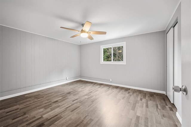 empty room featuring ceiling fan, light wood-type flooring, and wood walls