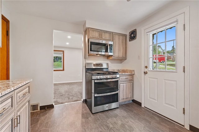 kitchen featuring light brown cabinets, light stone counters, dark carpet, and stainless steel appliances