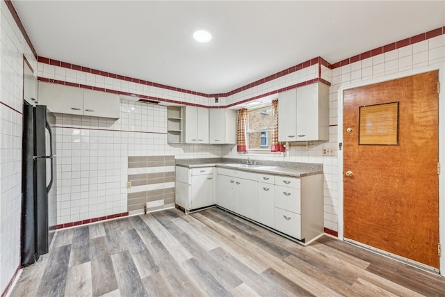 kitchen featuring black fridge, tile walls, light hardwood / wood-style floors, and white cabinetry