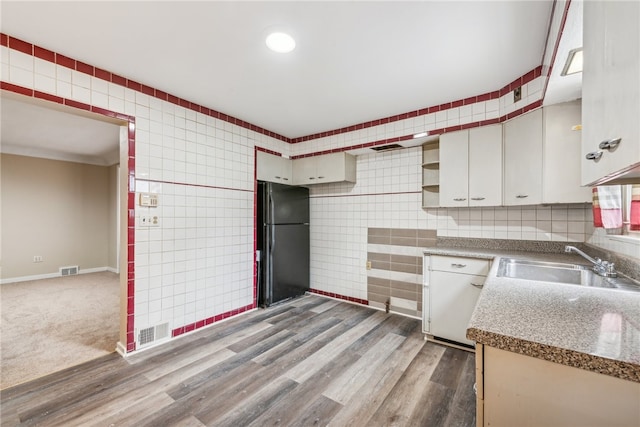 kitchen featuring tile walls, dark hardwood / wood-style floors, black fridge, sink, and white cabinets