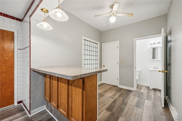 kitchen featuring pendant lighting, dark wood-type flooring, sink, kitchen peninsula, and ceiling fan