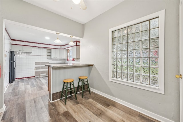 kitchen with ceiling fan, white cabinets, kitchen peninsula, a breakfast bar, and black refrigerator