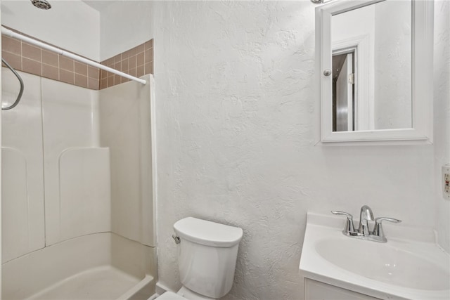 bathroom featuring a tile shower, vanity, and toilet