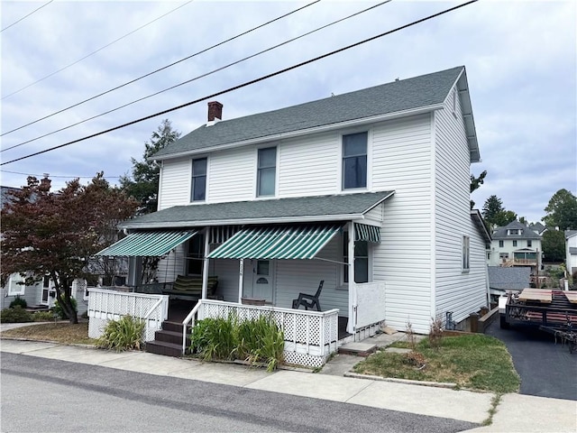 view of front of property with roof with shingles, a porch, and a chimney