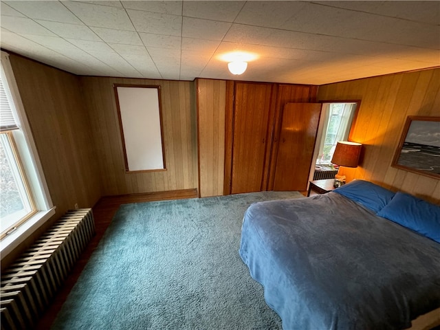 carpeted bedroom featuring radiator heating unit and wood walls