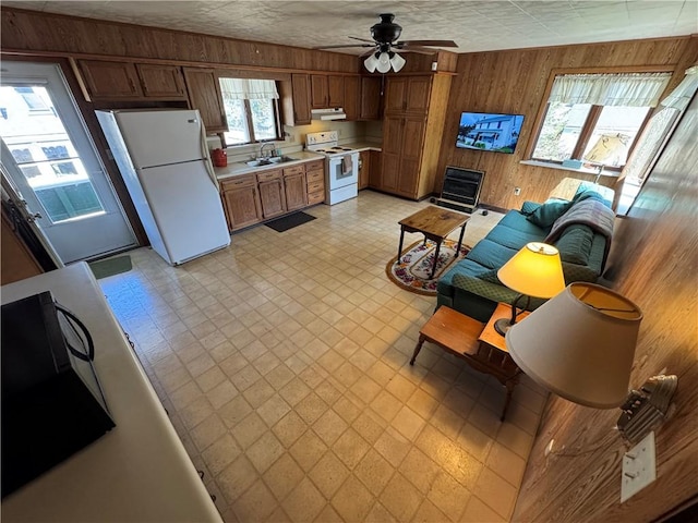 kitchen featuring white appliances, under cabinet range hood, wood walls, light countertops, and a sink