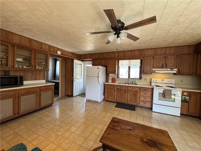 kitchen featuring white appliances, wooden walls, light countertops, under cabinet range hood, and a sink