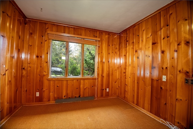 carpeted spare room featuring a baseboard radiator, wooden walls, and ornamental molding