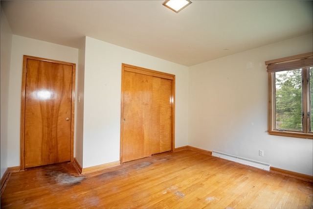 unfurnished bedroom with wood-type flooring, a baseboard radiator, and a closet