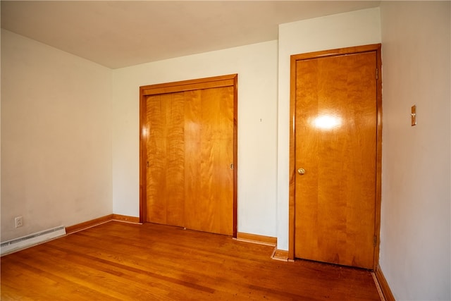 unfurnished bedroom with a baseboard heating unit and hardwood / wood-style flooring