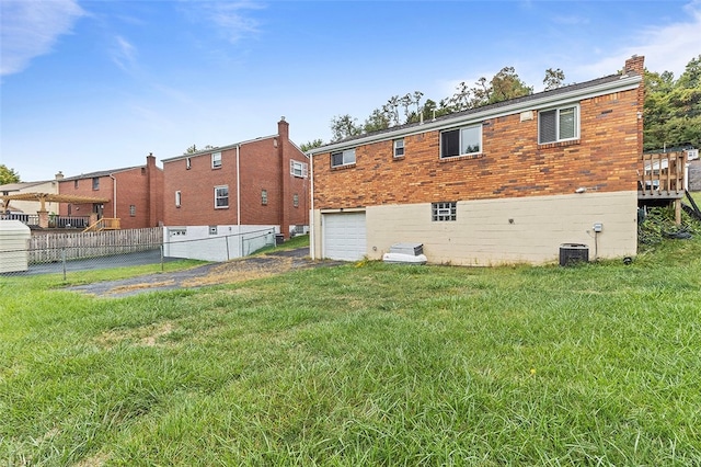 rear view of house featuring a garage, a yard, and central AC