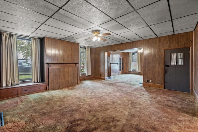 unfurnished living room featuring carpet, a drop ceiling, wood walls, and ceiling fan