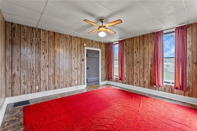 unfurnished room with ceiling fan, wooden walls, and a healthy amount of sunlight