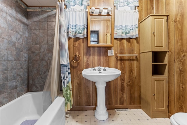 bathroom featuring shower / bath combo with shower curtain, wooden walls, and toilet