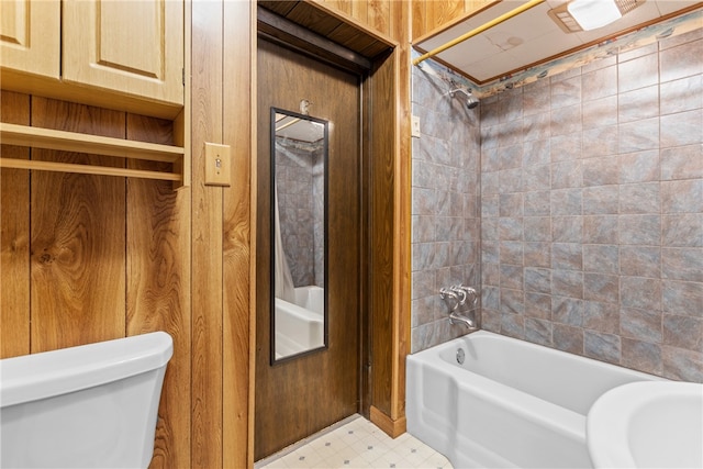 bathroom featuring wood walls, tiled shower / bath, and toilet