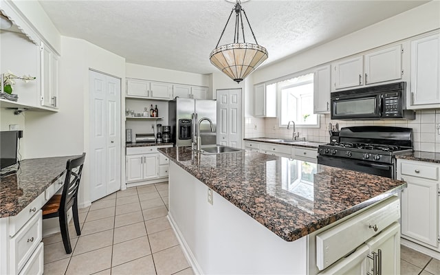 kitchen featuring white cabinetry, an island with sink, black appliances, dark stone counters, and sink