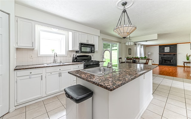 kitchen with white cabinets, a fireplace, black appliances, a kitchen island with sink, and sink