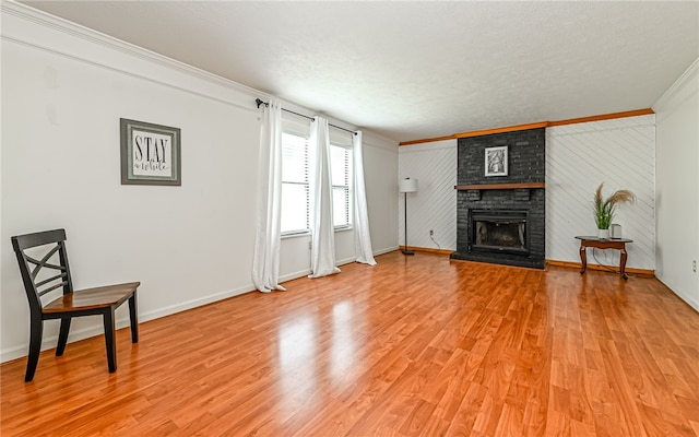 living room with a brick fireplace, light hardwood / wood-style floors, a textured ceiling, and crown molding