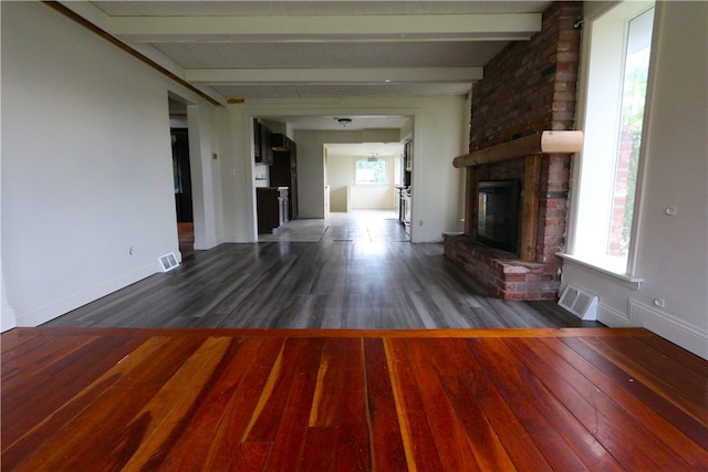 unfurnished living room featuring a brick fireplace, beam ceiling, and dark wood-type flooring