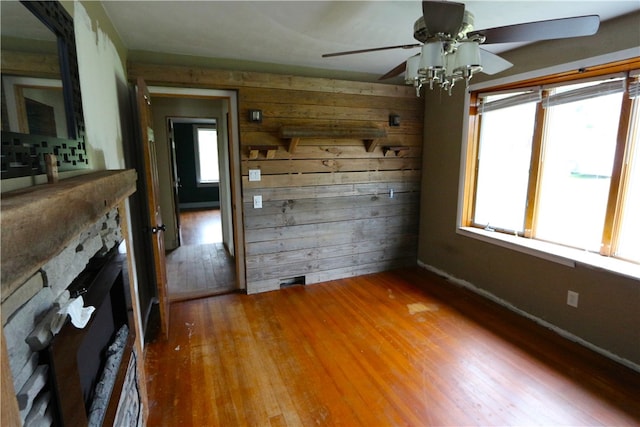 unfurnished living room featuring wooden walls, hardwood / wood-style floors, ceiling fan, and a fireplace