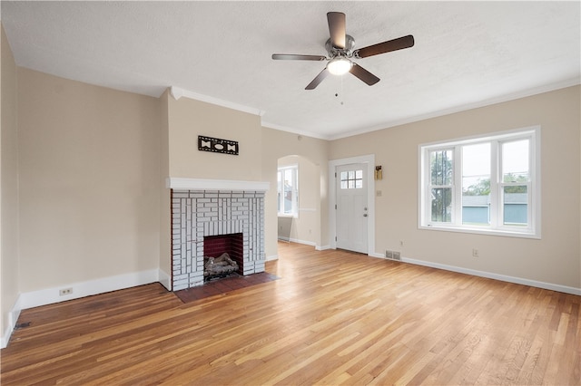 unfurnished living room featuring a textured ceiling, light hardwood / wood-style floors, a fireplace, crown molding, and ceiling fan