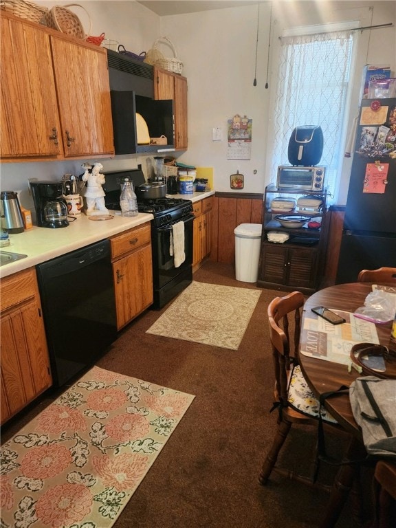 kitchen featuring black appliances, wooden walls, and dark carpet