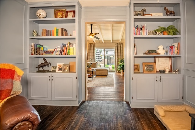 interior space featuring built in shelves, ceiling fan, beamed ceiling, and dark wood-type flooring